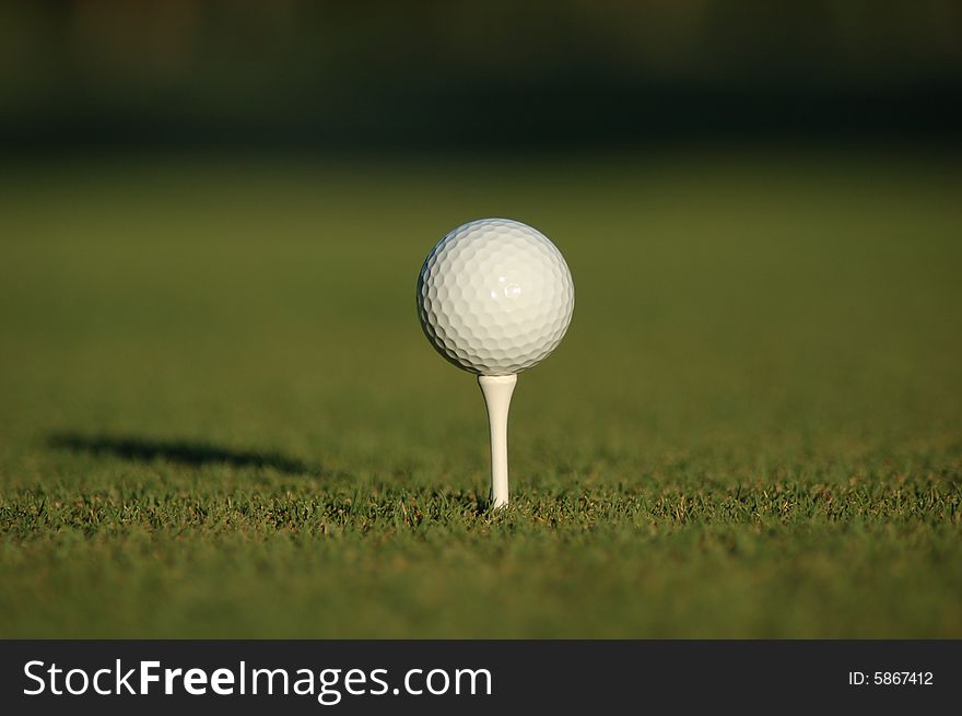 A white golf ball sitting on a white tee with blurry fairway in the background. A white golf ball sitting on a white tee with blurry fairway in the background.