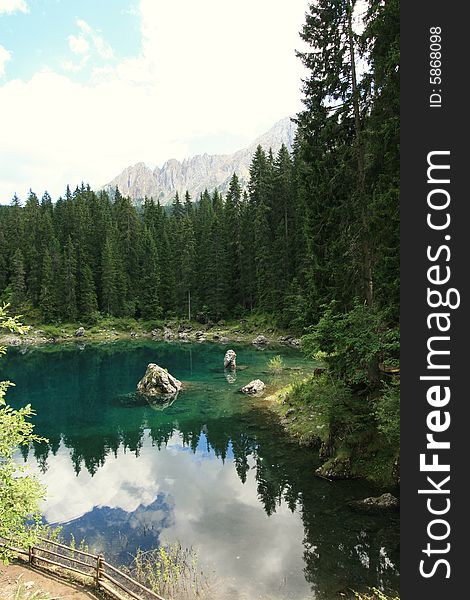 Green pines woods, blue turqoise Carezza  lake & view on Sella montain group, Italy. Green pines woods, blue turqoise Carezza  lake & view on Sella montain group, Italy