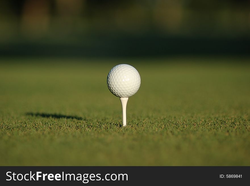 A white golf ball sitting on a white tee with blurry fairway in the background. A white golf ball sitting on a white tee with blurry fairway in the background.
