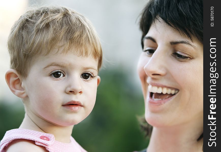 Sweet baby girl in the arms of a happy smiling mother outdoors. Sweet baby girl in the arms of a happy smiling mother outdoors