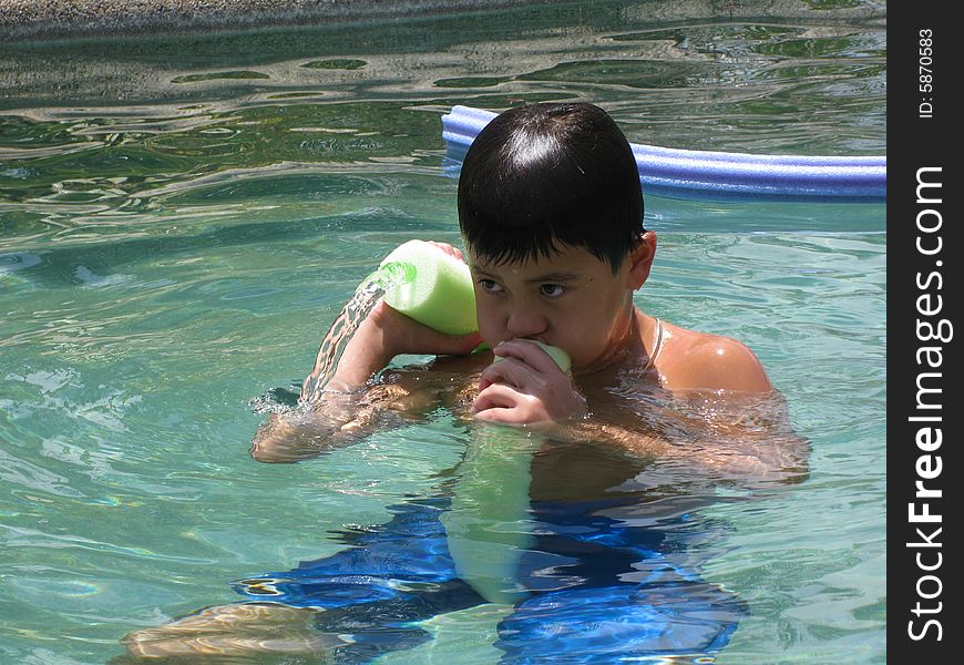 Dark haired boy in swimming pool shooting water through a pool toy. Dark haired boy in swimming pool shooting water through a pool toy