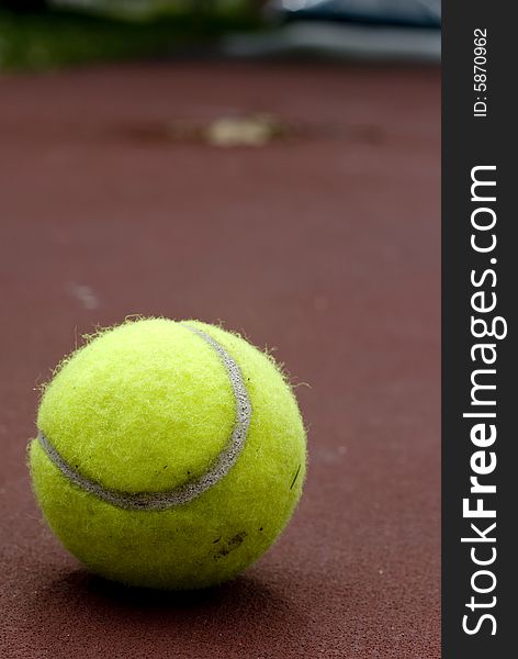 A tennis ball laying near a fence of the tennis courts.