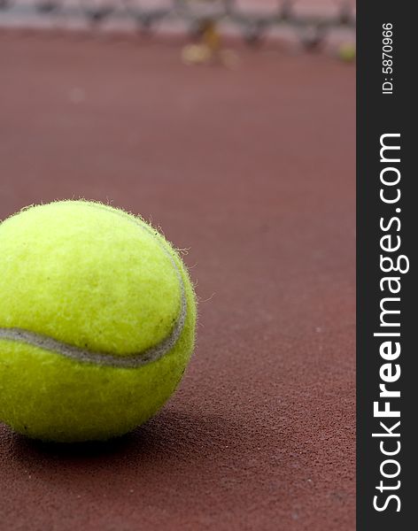 A tennis ball laying near a fence of the tennis courts.