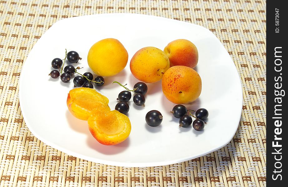 Ripe apricots and black currant on a white plate. Ripe apricots and black currant on a white plate