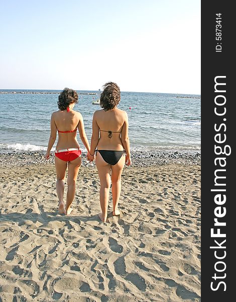 Two pretty sisters on the beach walking to the sea. Two pretty sisters on the beach walking to the sea.