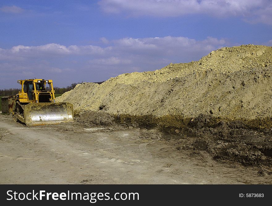 The robust bulldozer and the large mound of dirt hill. The robust bulldozer and the large mound of dirt hill