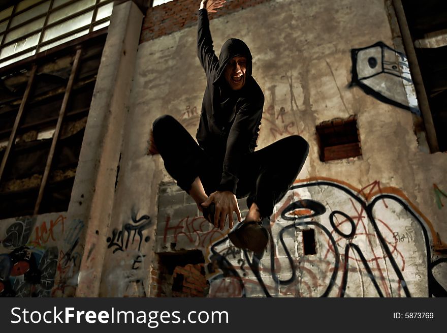 The person in black jumps inside of the thrown building with graffiti. The person in black jumps inside of the thrown building with graffiti