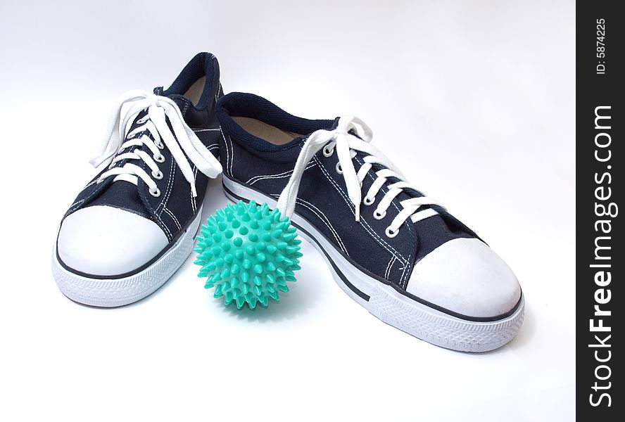 Black-and-white classical gym shoes and green ball on a white background. Black-and-white classical gym shoes and green ball on a white background