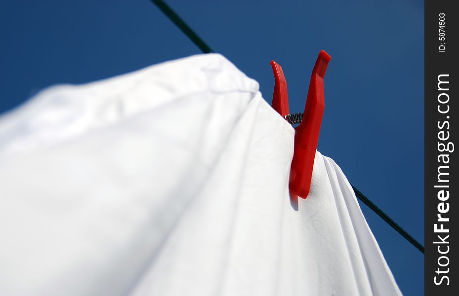 Solitary red clothes peg keeps a firm hold on white laundry, shouting: Look at me; I'm in control!