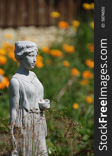 Garden statue of girl waits with a cup in her hand against an out-of-focus background of orange fllowers. Garden statue of girl waits with a cup in her hand against an out-of-focus background of orange fllowers