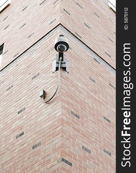 Mounted on the corner of a brick wall, a bubble-glass overhead security camera observes its surroundings. Mounted on the corner of a brick wall, a bubble-glass overhead security camera observes its surroundings.