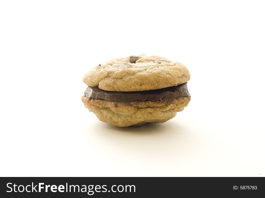 A chocolate chip cookie sandwiches with chocolate filling on a white backdrop.
