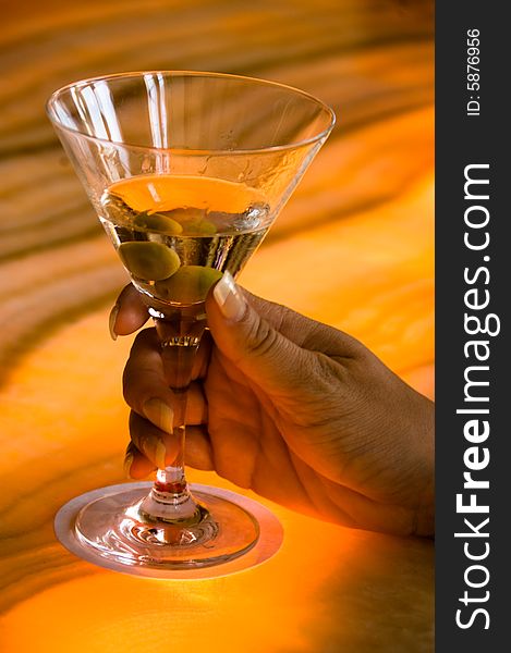 Dirty Martini with green olives, held by a woman's hand on a colorful bar countertop. Dirty Martini with green olives, held by a woman's hand on a colorful bar countertop