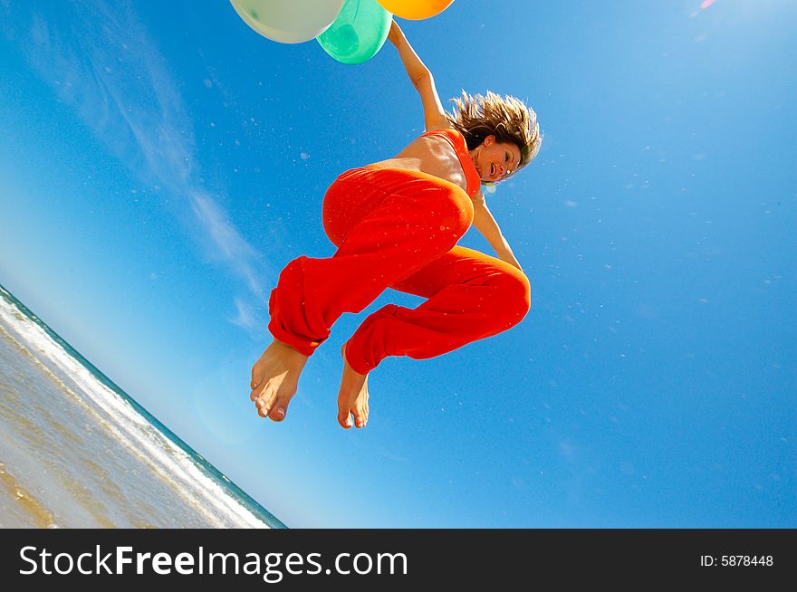 Girl with colorful balloons jumping on the beach