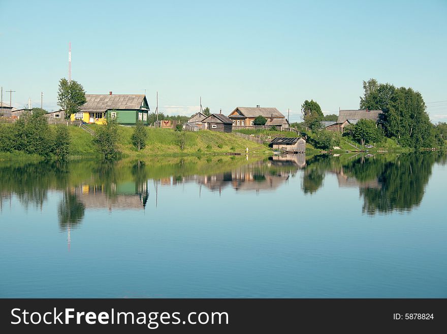 Village on the bank of the river and its reflection in the water