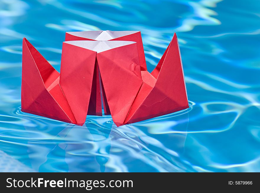 Red paper ship sailing on a blue water of a pool