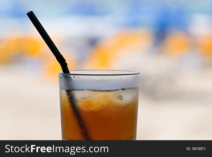 Glass of cold ice tea on table with blurred beach in background. Glass of cold ice tea on table with blurred beach in background