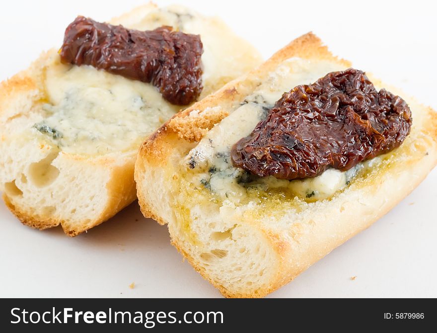 Sun dried tomatoes on melted stilton blue cheese on toasted baguette, isolated on white background