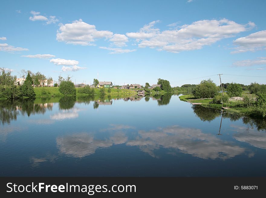 Village on the bank of the river and its reflection in the water