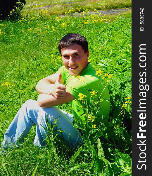 The young man on a grass, shows the big finger.
