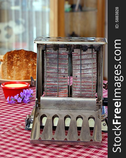Vintage, working toaster with red elements on a table with toast, butter and flowers. Vintage, working toaster with red elements on a table with toast, butter and flowers.