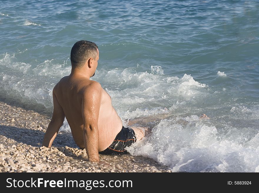 Man relaxing in the water on the beach looking at sea waves