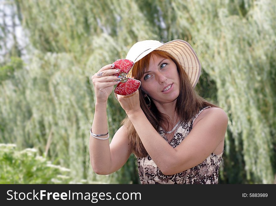 Woman look at oneself in the small mirror. A green tree branches on the smear background.