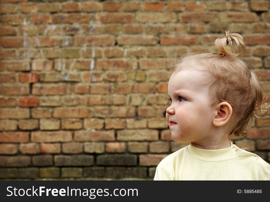An image of baby-girl near a yellow brick wall