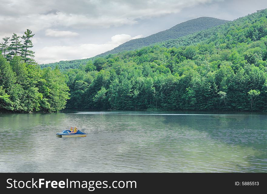 One of Vermonts wonderful lakes shows the shimmering color of emerald and the reflections of trees and clouds on the water as 2 children are enjoying the use of a a paddle boat on  the water. One of Vermonts wonderful lakes shows the shimmering color of emerald and the reflections of trees and clouds on the water as 2 children are enjoying the use of a a paddle boat on  the water