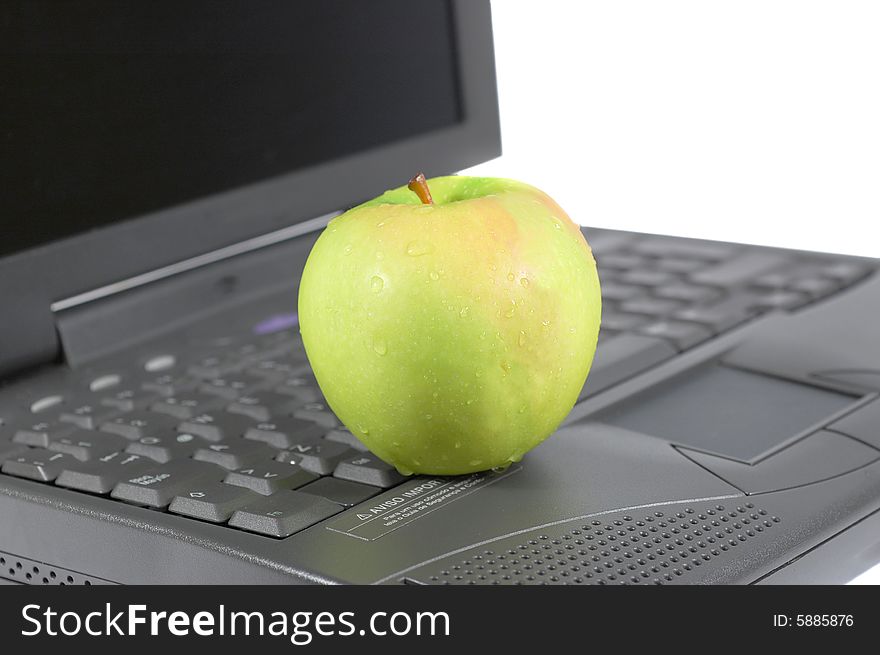 A green apple on top of a laptop. A green apple on top of a laptop