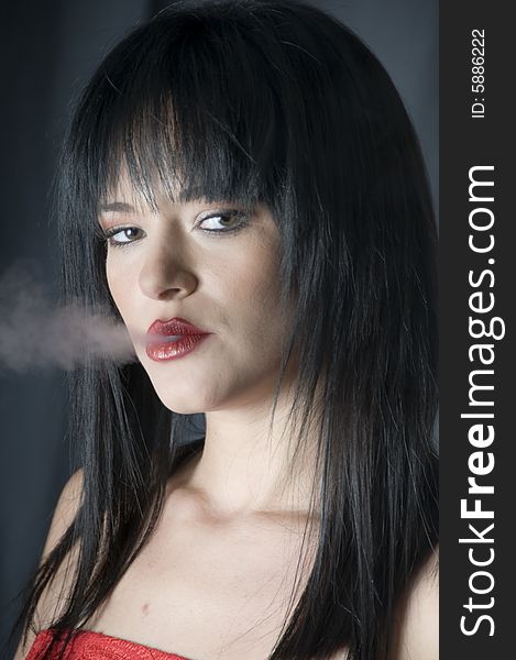A head and shoulders portrait of a young lady with red lipstick exhaling smoke from a cigarette. A head and shoulders portrait of a young lady with red lipstick exhaling smoke from a cigarette