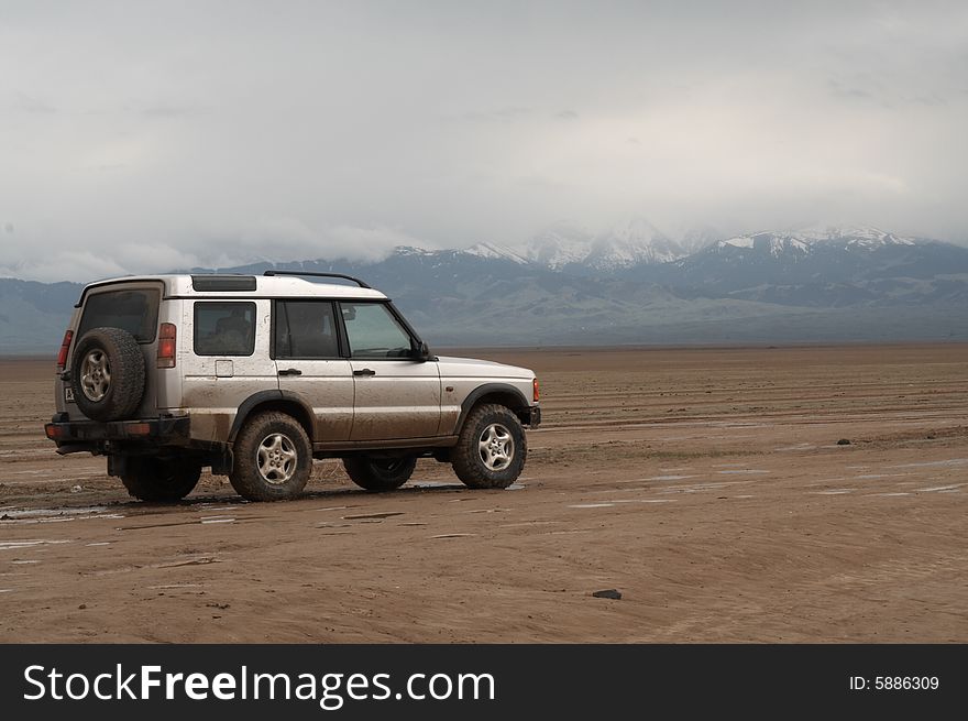 SUV trek across a steppe after the rain, snow mountains on background