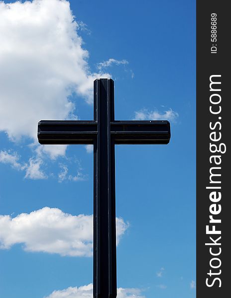 Black metal cross on a cloudy blue sky background. Black metal cross on a cloudy blue sky background