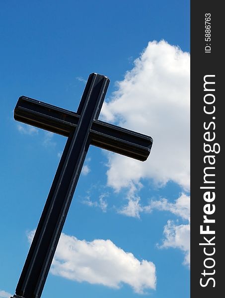 A black cross on a blue cloudy sky background. A black cross on a blue cloudy sky background