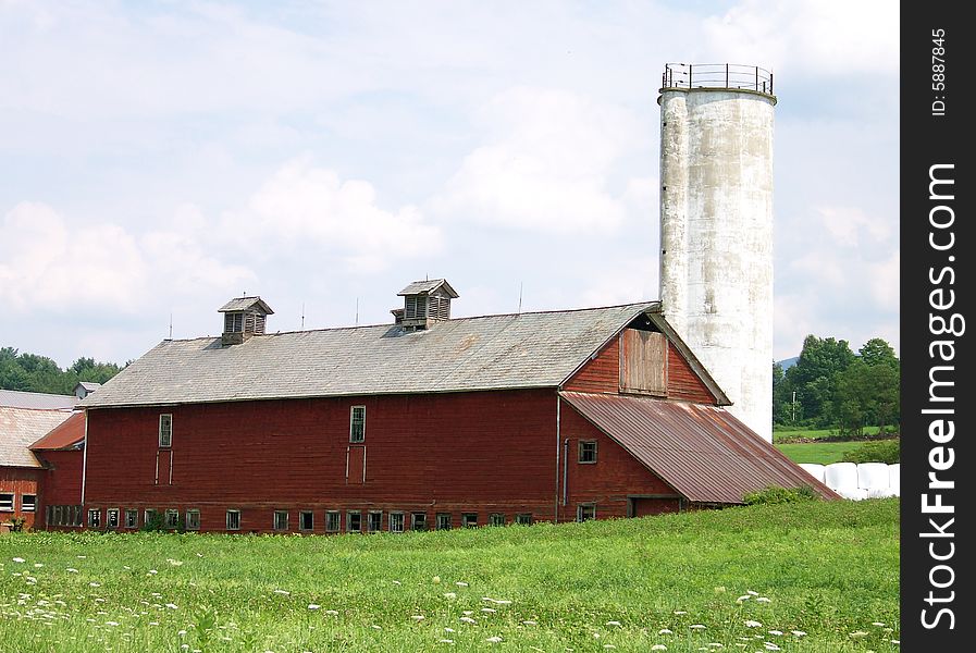 A beautiful well kept Vermont Barn sits in a field with a very unusual silo.