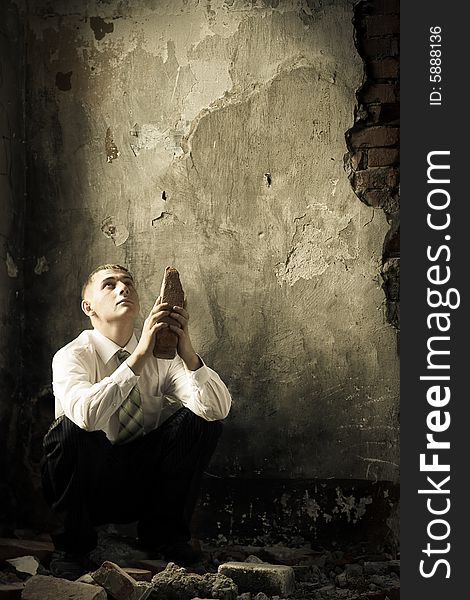 Sitting sad young businessman and holding obsolete brick, copy space for the text