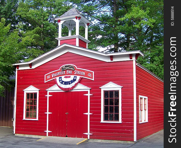 A little replica of a fire station stands colored in 
bright red and white in the afternoon sunshine.