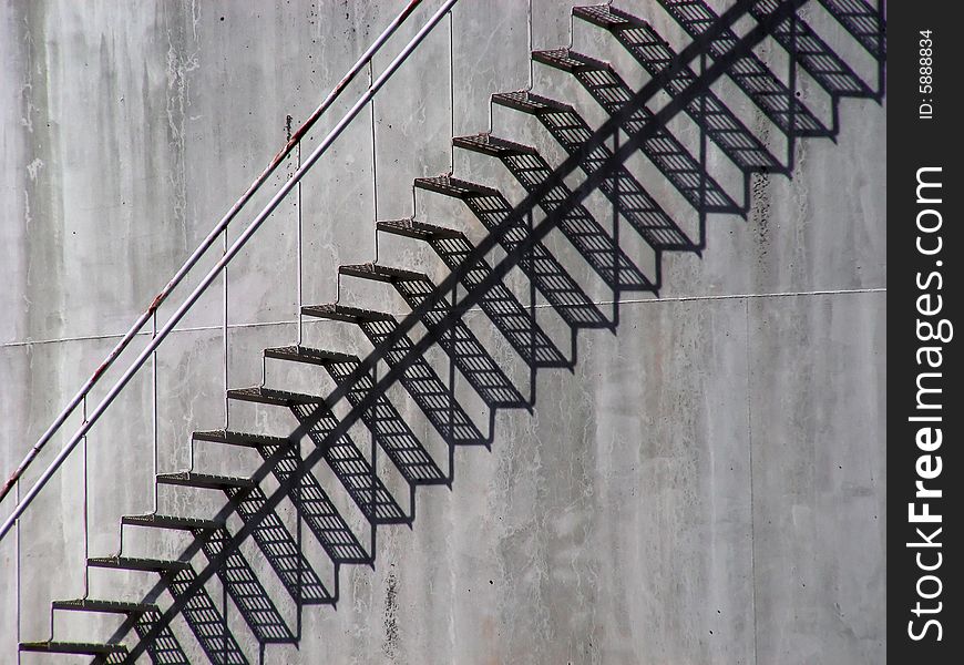 Sunlight makes a shadow pattern of steps on the side of a huge oil storage tank.