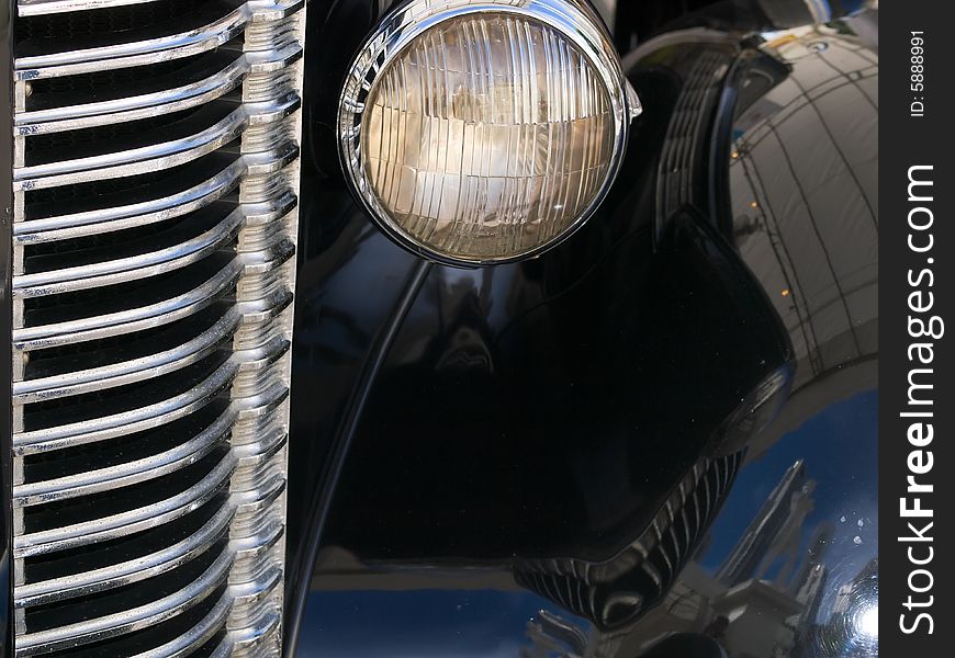 Close up of radiator grille and headlights of vintage black car with reflective shiny surface. Close up of radiator grille and headlights of vintage black car with reflective shiny surface