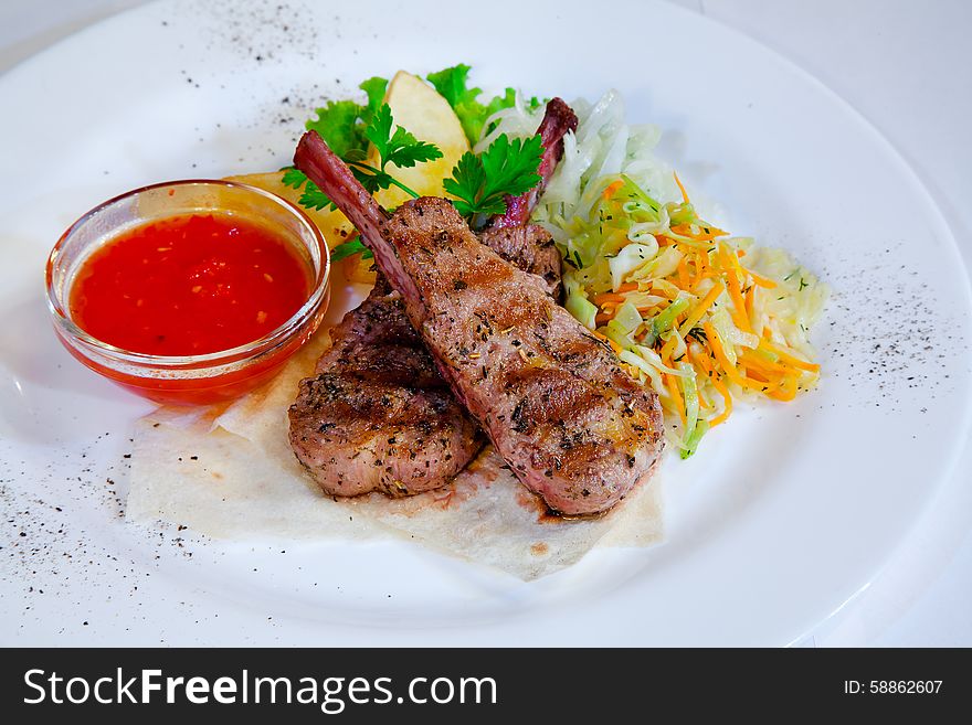 Roasted meat with vegetables and spicy sauce on the plate closeup