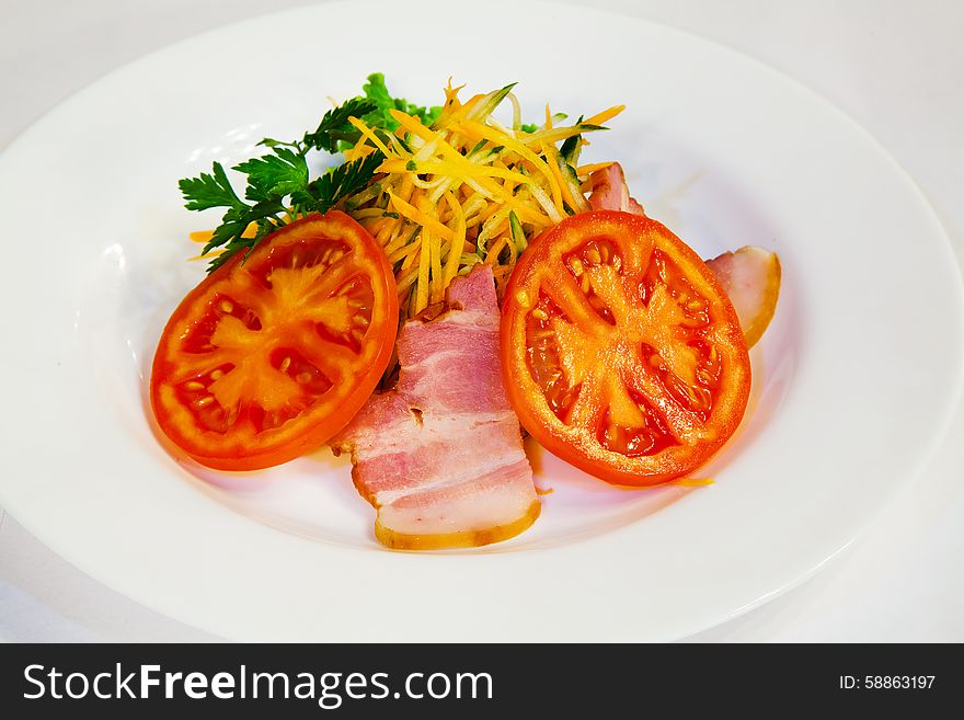 Fresh carrot salad with bacon and tomatoes on the plate closeup