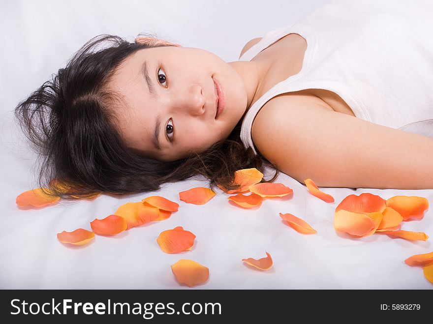 Young asian female is lying on white background with fallen orange petals. Young asian female is lying on white background with fallen orange petals