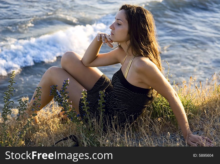 Pretty young woman sitting on the grass beside the sea. Pretty young woman sitting on the grass beside the sea