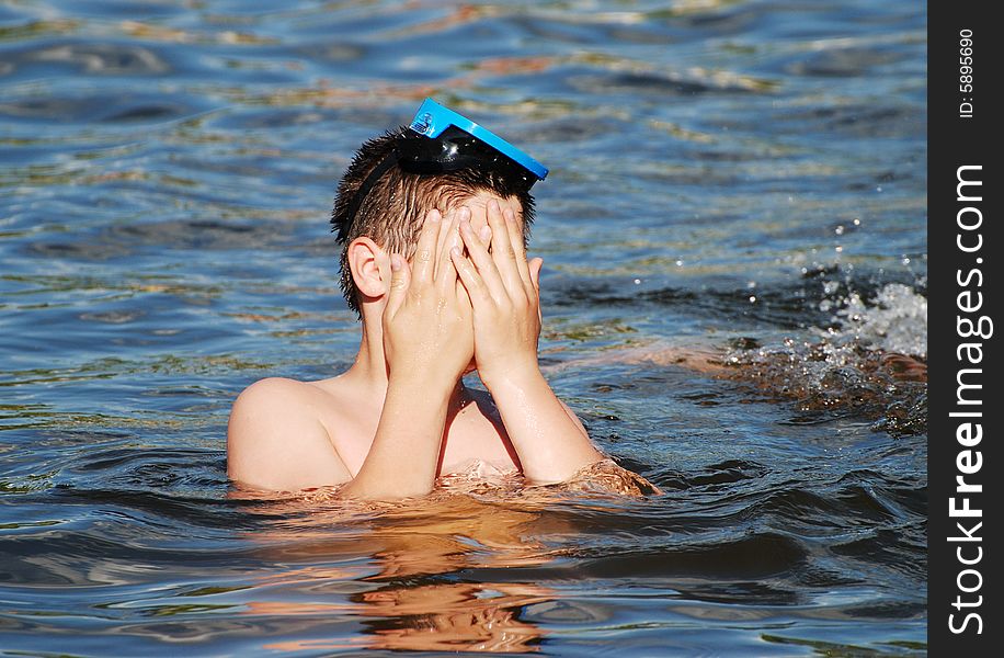 The boy is covering his face with hands in a small lake late afternoon. The boy is covering his face with hands in a small lake late afternoon.