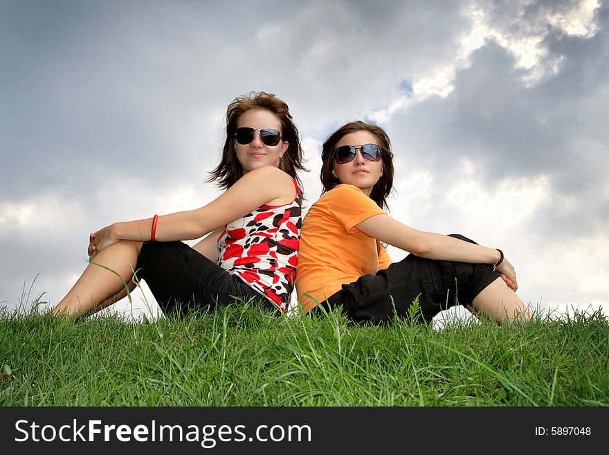 Friends sitting on the grass against cloudy sky