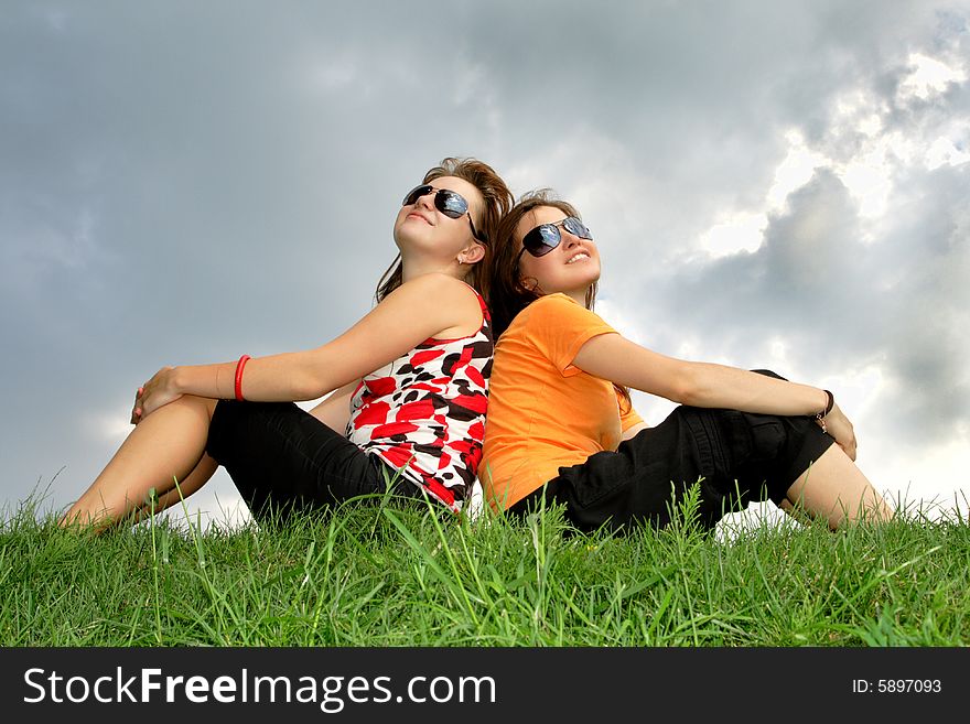 Friends sitting on the grass against cloudy sky