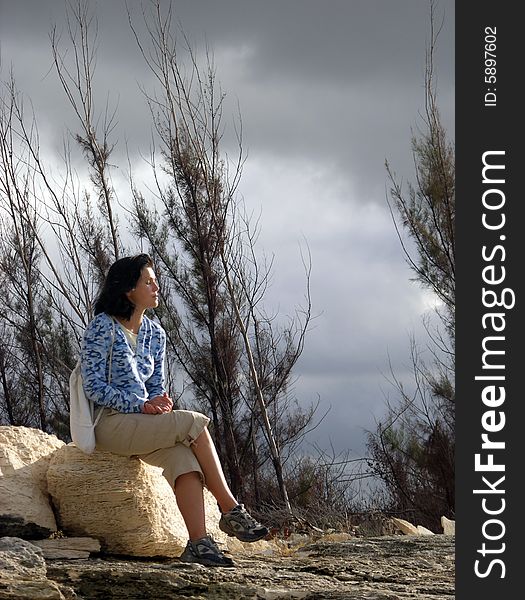 The girl sitting on a stone and the cloudy dark sky in a background on Grand Bahama Island, The Bahamas.