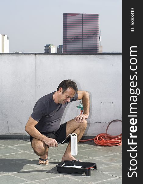 Smiling man squatting with hand on knee holding paint roller. He is looking at the paint roller. Vertically framed shot. Smiling man squatting with hand on knee holding paint roller. He is looking at the paint roller. Vertically framed shot.