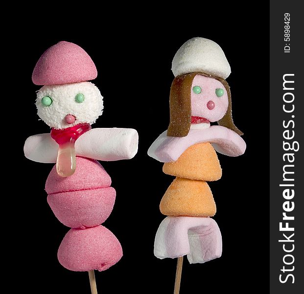 A male and a female figurine made out of candies on a stick over a black background. A male and a female figurine made out of candies on a stick over a black background.