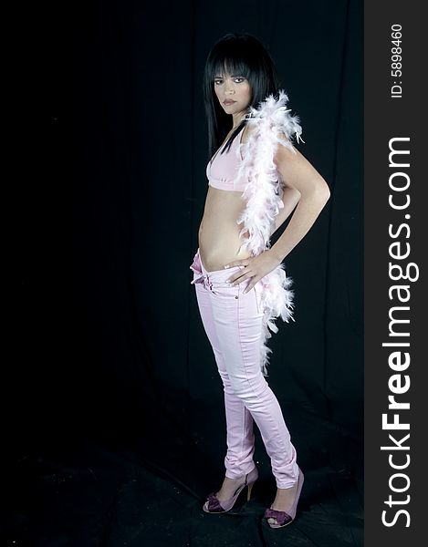 Full length of a young woman dressed in pink denims, a pink top and boa and purple shoes. She has black hair and pink lipstick. Full length of a young woman dressed in pink denims, a pink top and boa and purple shoes. She has black hair and pink lipstick.